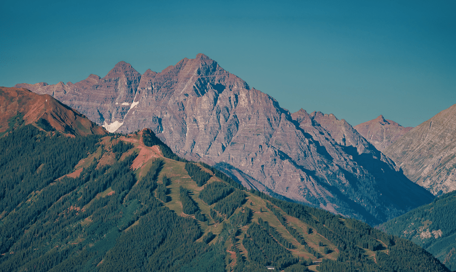 Aspen Highlands in the summer, green slopes and red, stark mountains in the distance