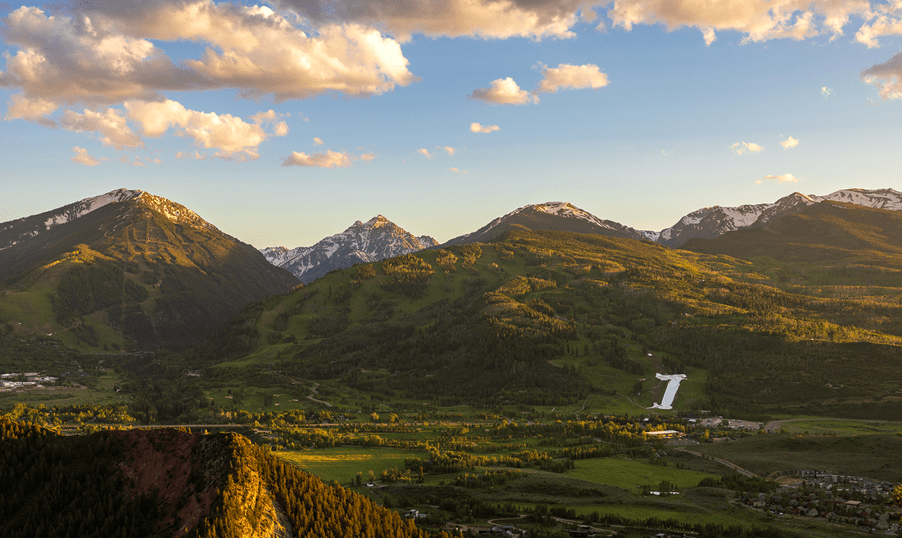 Buttermilk in early summer, the valley is green as the sun casts a golden glow, but a single strip of the snowy half pipe can still be seen from afar