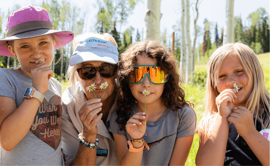 Three little girls and a woman hold small wildflowers up to their noses and pose for the camera