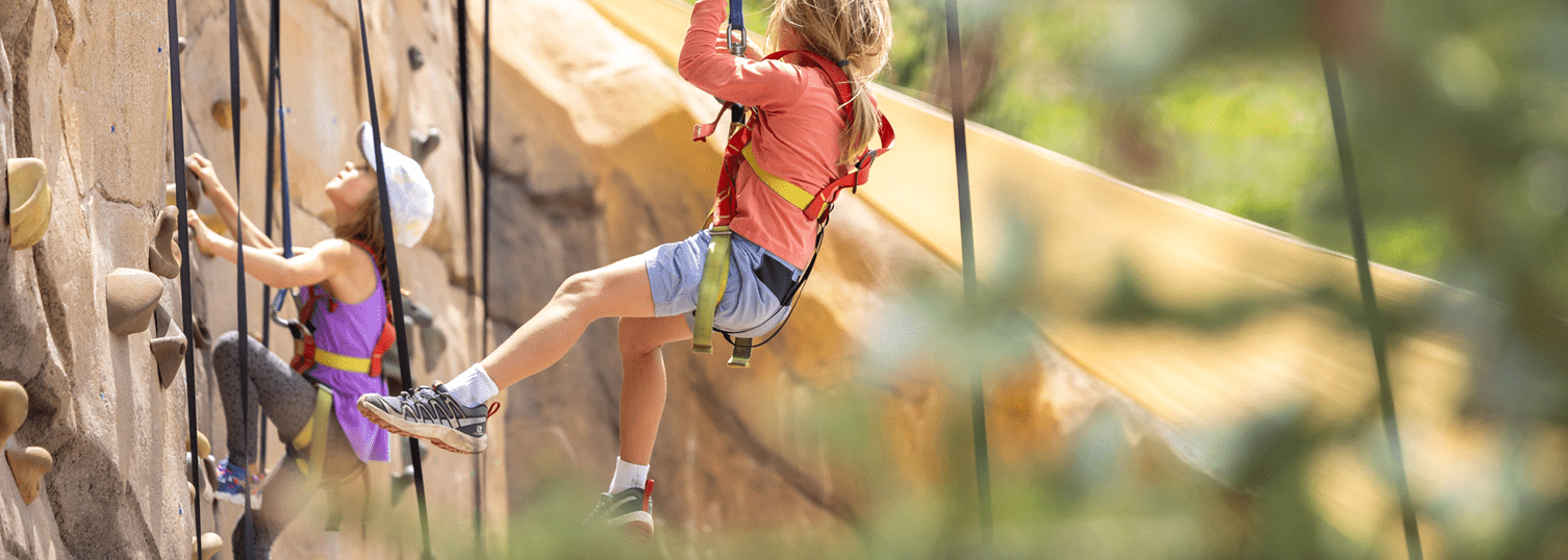 Two little girls climb on the outdoor climbing wall at Camp Aspen Snowmass