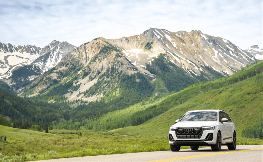 White Audi drives through rolling green hills below blue skies during the summer months of aspen