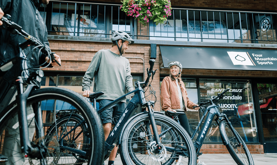 Couple smile at each other as they stand next to their rented ebike from Four Mountain Sports 