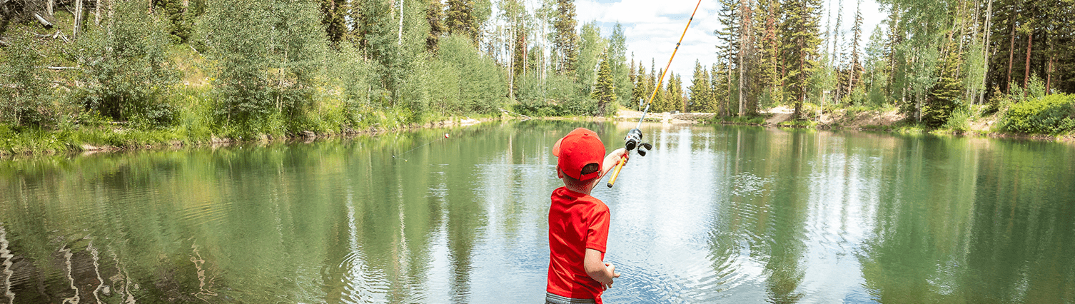 Boy in all red casts his line into the water of the pond atop Snowmass