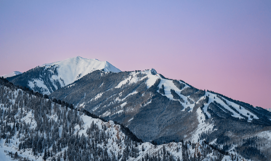 Pink and purple skies over aspen highlands ski resort, covered in snowy runs and deep green pine trees
