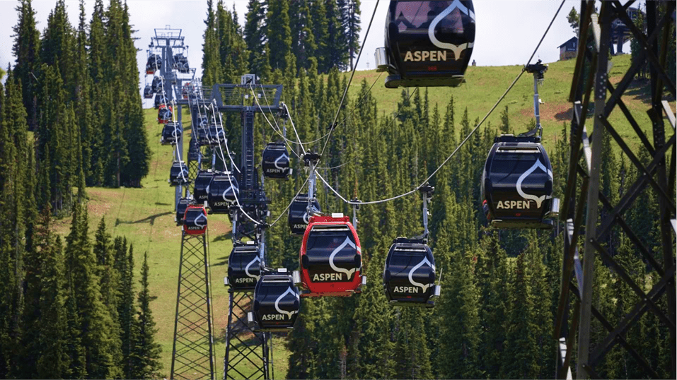 Gondolas travel along the silver queen cable line in summer at snowmass over green pine trees and ski runs