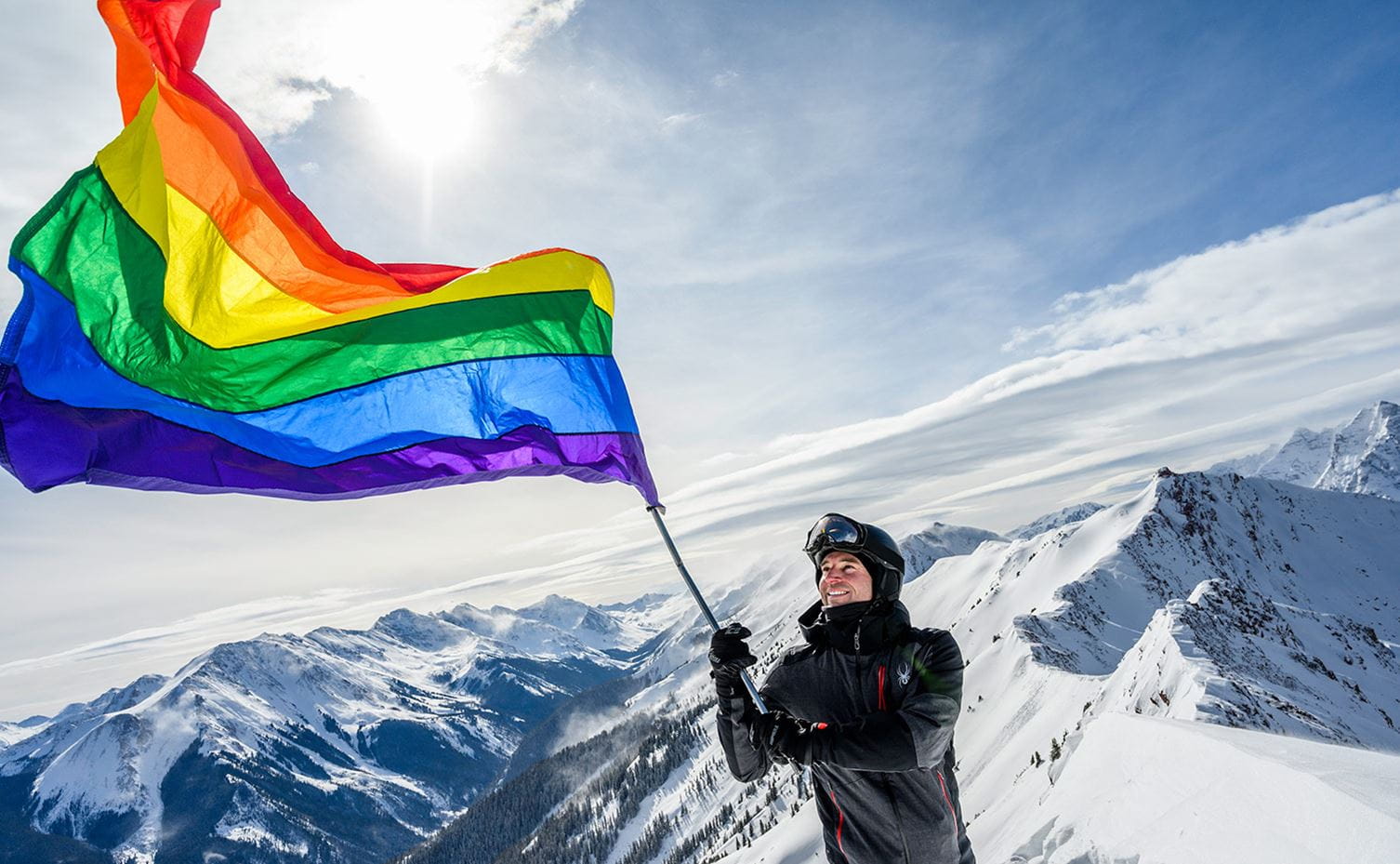 A man waves a rainbow flag from atop Highland Bowl at Aspen Snowmass to celebrate Gay Ski Week