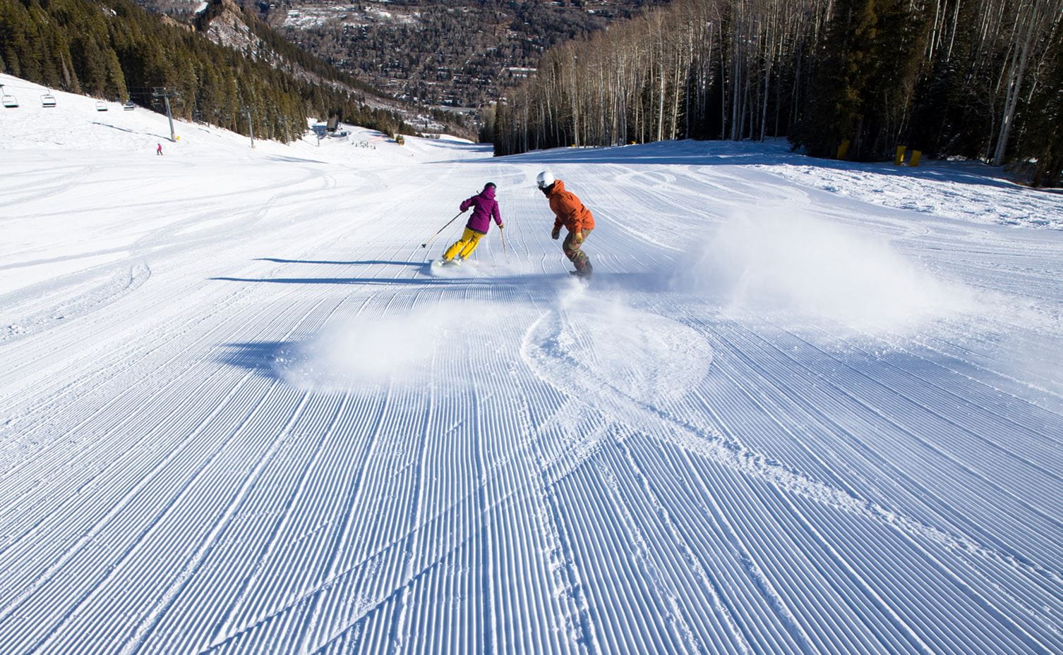 A skier and rider enjoy groomed terrain at Aspen Snowmass, Colorado - Ski with a Season Pass