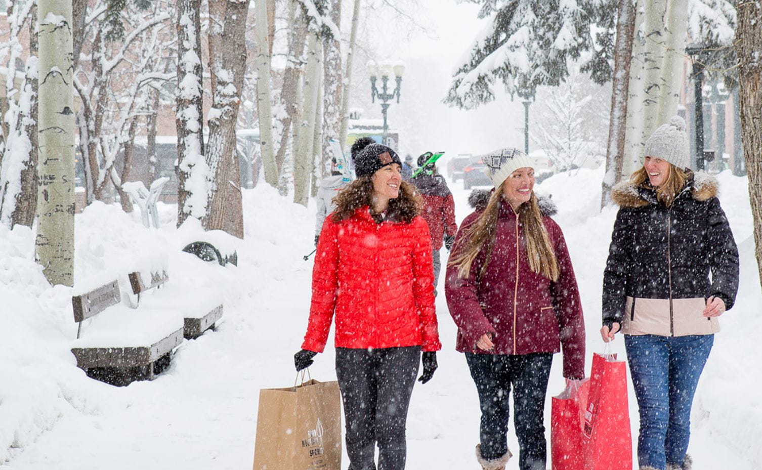 Three women walk down the streets of Aspen in winter with shopping bags