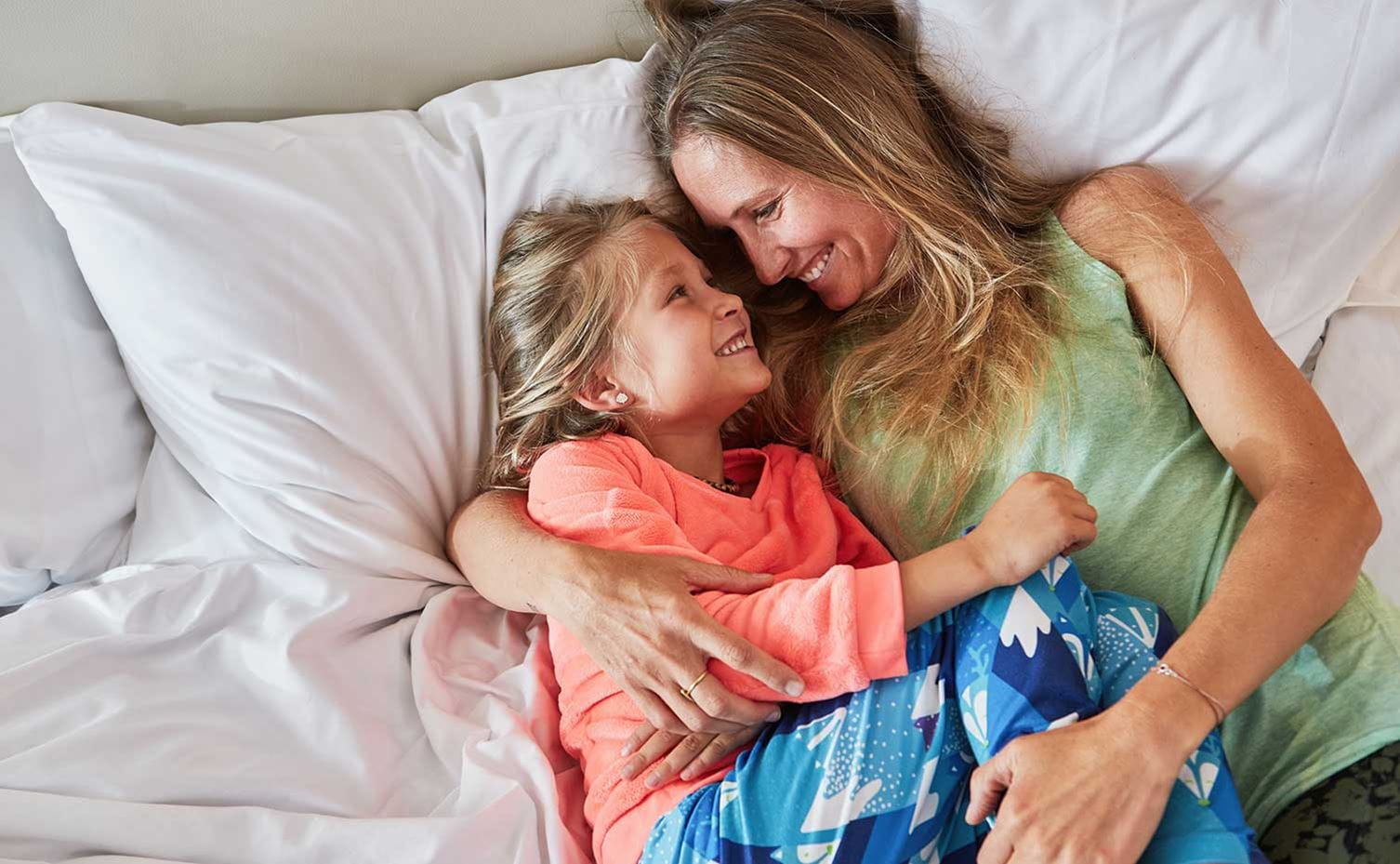 Mother and daughter snuggle in a bed at the Limelight Hotel Snowmass