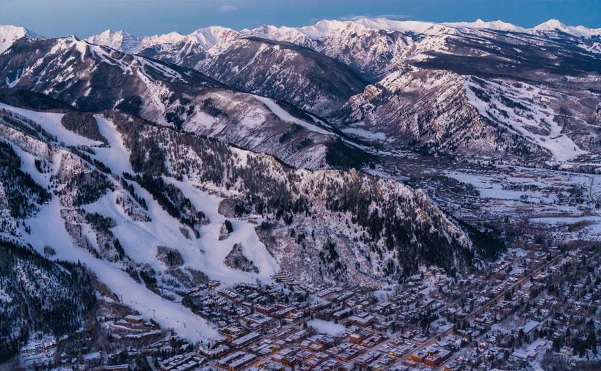 a snowy mountain range with buildings and trees