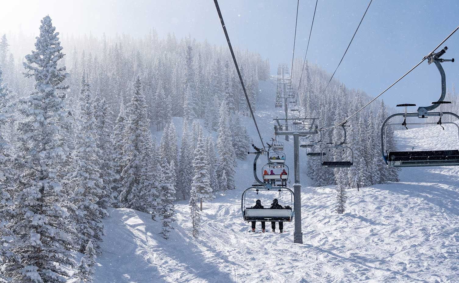 Skiers ride a lift up at Aspen Snowmass as the sun breaks through clouds