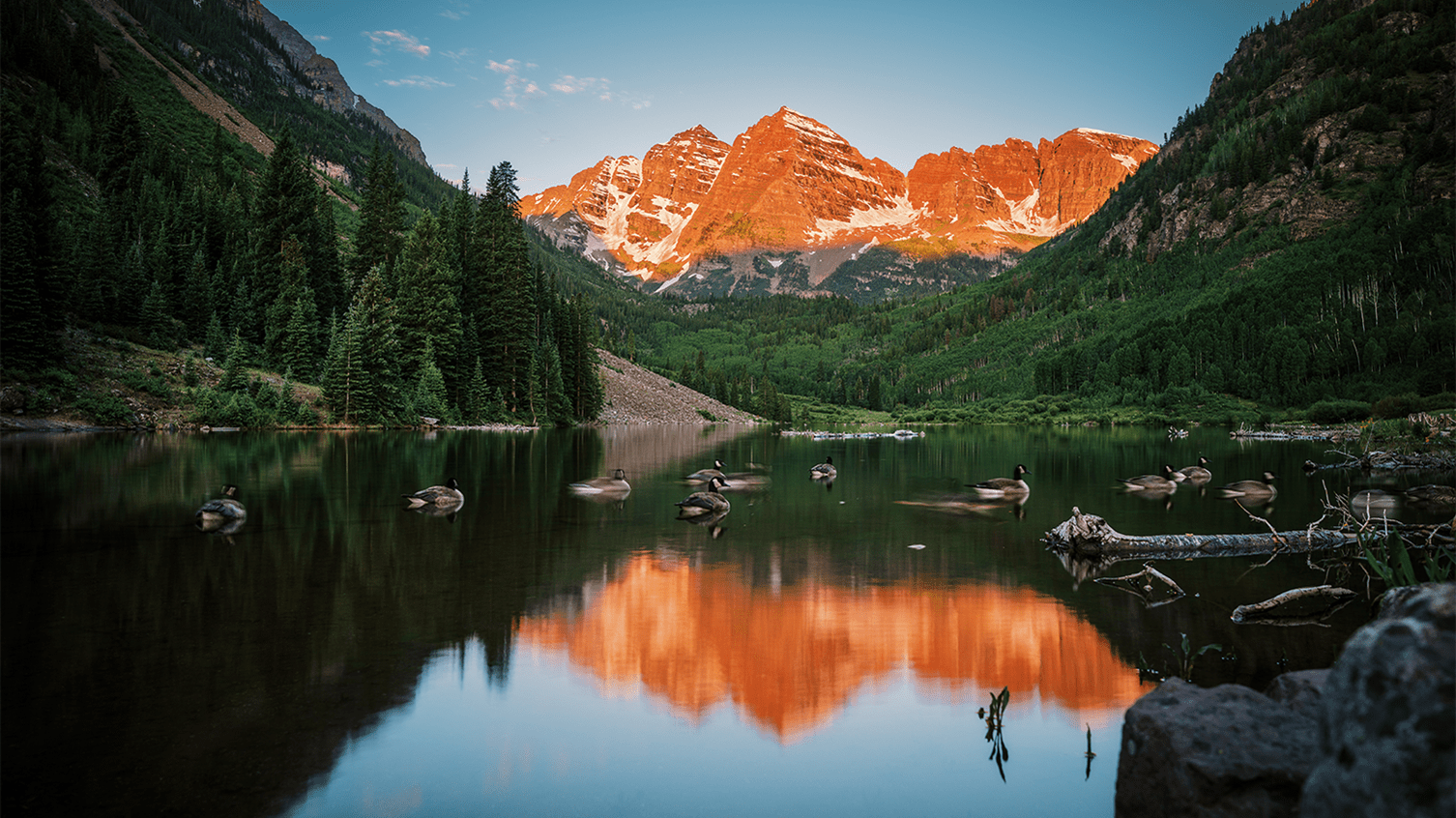 Dawn sun hits the Maroon Bells, Geese swim in the shade in the lake at the base