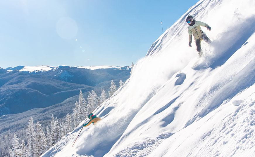 A snowboarder and skier descend the steeps at Aspen Mountain
