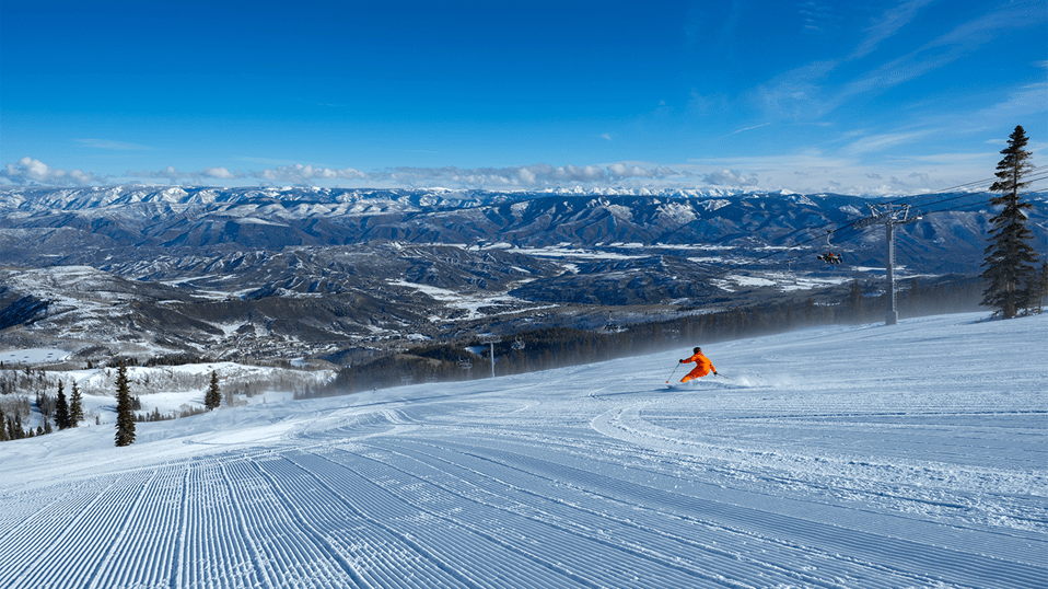 Skier carves through fresh corduroy on a blue bird day at Snowmass, the Roaring Fork Valley stretches out in background 