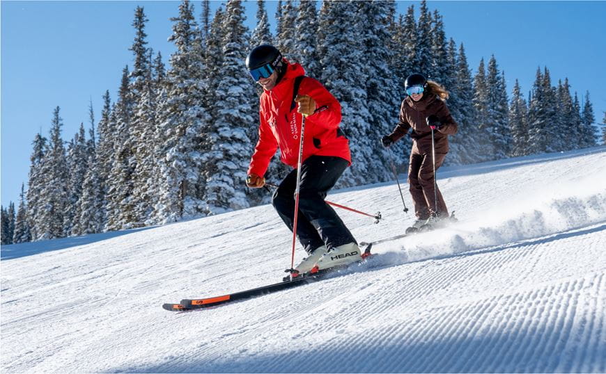 A skier with a ski pro skiing down the mountain
