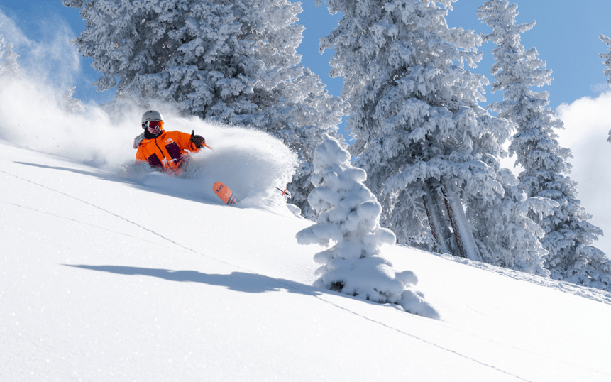 Skier in orange jacket skiing through perfect powder on a blue sky day