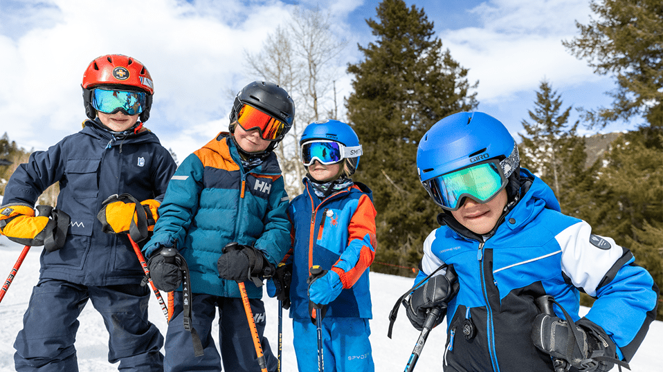 Four kids smile at the camera as they ski together on Aspen Highlands