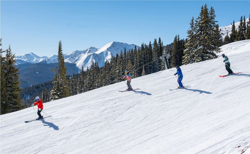 3 skiers with a skier pro taking a group lesson on Aspen Mountain
