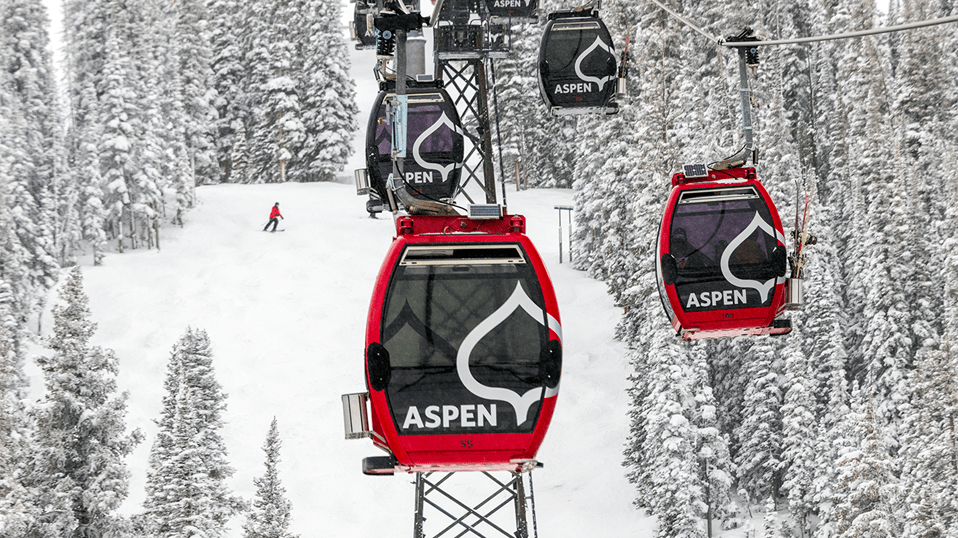 Silver Queen Gondola over fresh snow on the trees of Aspen Mountain, skier makes turns below