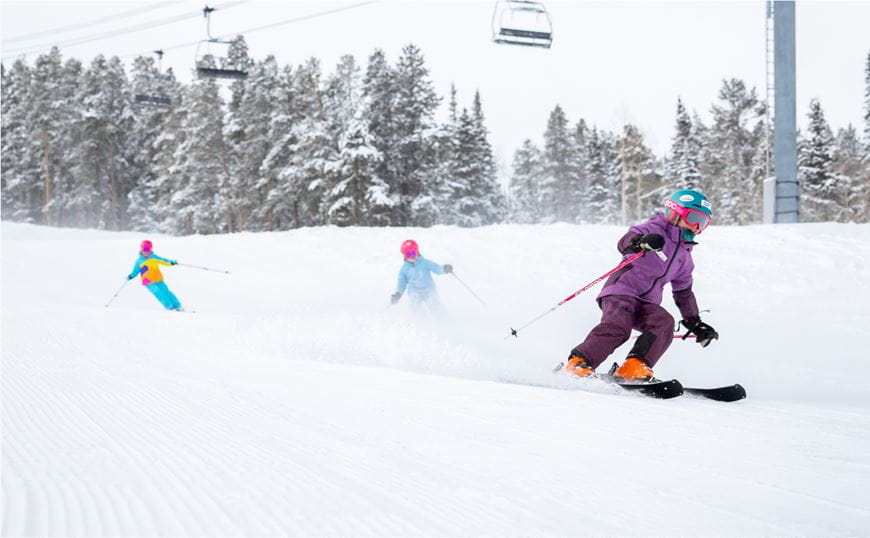 Children skiing down a snowy slope under a chairlift