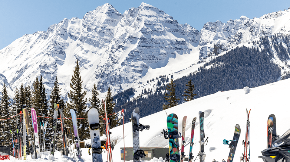Skis and snowboards stuck into the snow at Buttermilk, in Aspen, with Maroon Bells in background
