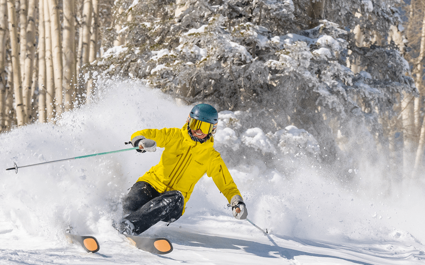 Skier in yellow jacket skiing through powder in the trees at Aspen Snowmass