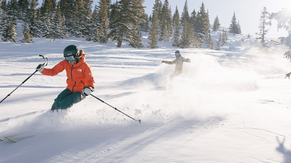 Two skiers glade down deep powder on a bright sunny morning, on a winter day, at Aspen Snowmass
