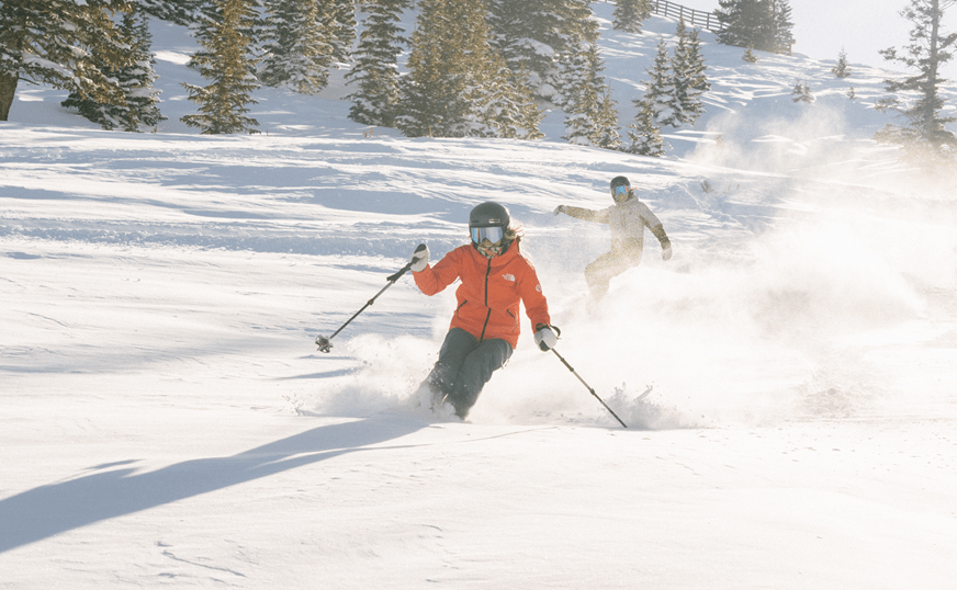 Skier and snowboarder cutting through powder at Aspen Snowmass ski resort