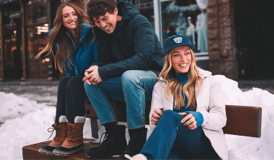 Three people sit on a bench in Aspen in their Aspen Collection clothing, on a snowy winter day