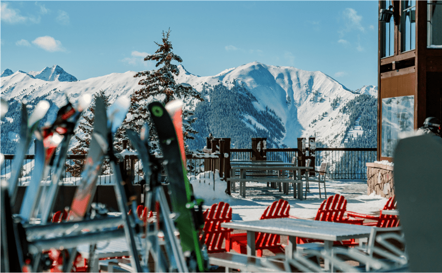 View of Sundeck on Aspen Mountain, skies on rack and snowy peaks behind the sun soaked porch
