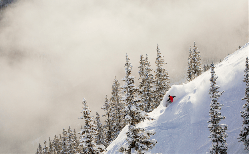 Ariel view of a skier carving through powder, mist atop mountains tops and snow covered trees