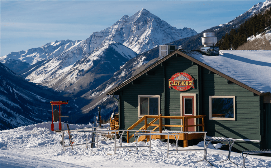 Buttermilk mountain lodge in the morning, the rustic green cabin is highlighted by the stunning, snow capped maroon bells behind