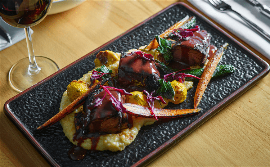 winter roasted veggies over grits, on fancyy blue plate with glass of red wine next to plate