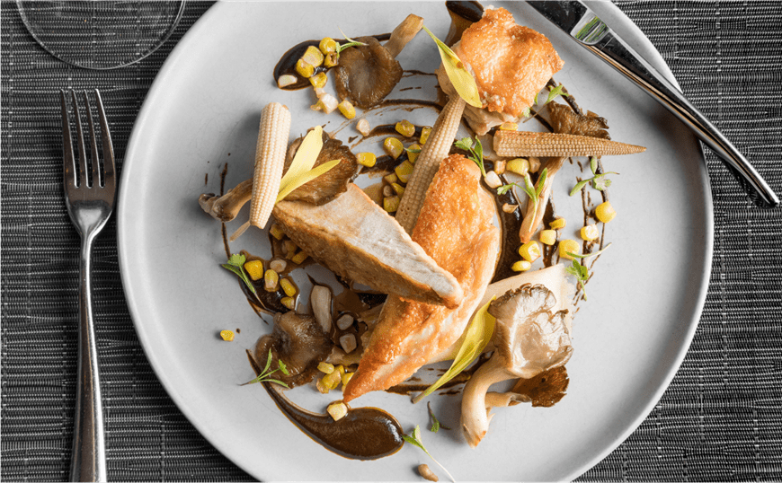 Fine dining dish of chicken, baby corn, and greenery skillfully plated on a white plate at Element 47 in Aspen Colorado