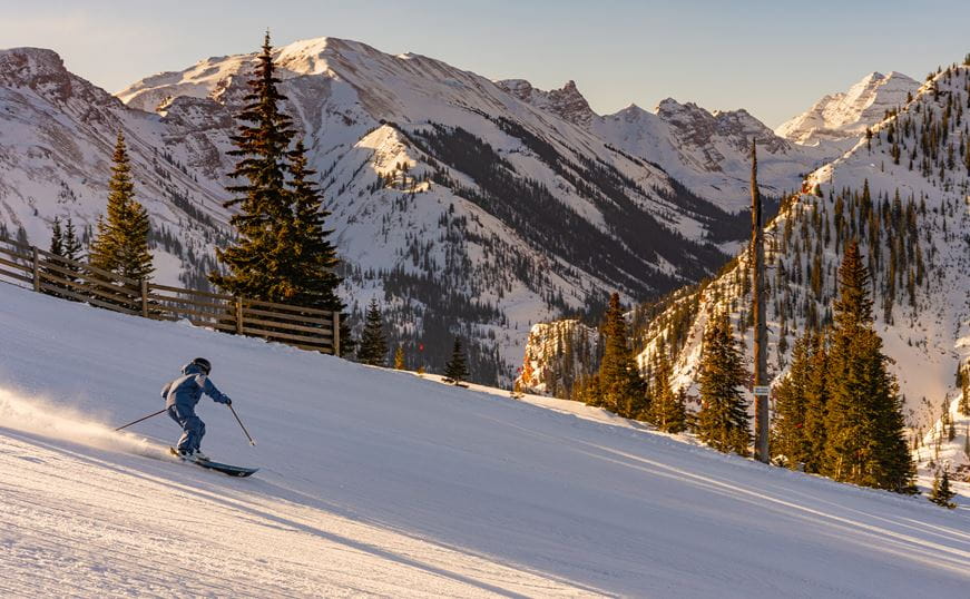 Single skier carves down an empty slope, golden lights casting on the ski slopes and trees