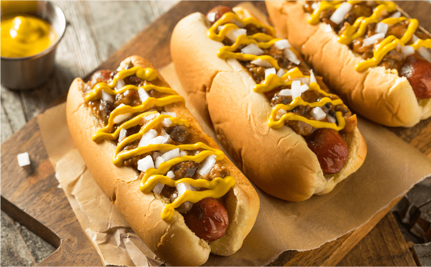 Close up image of three hotdogs with mustard and onions stacked on parchment paper, on a wodden table at Snowmass Ski resort