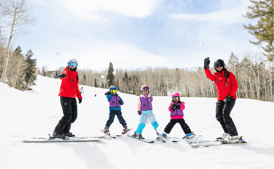 Two instructors and three children throw snowballs at the camera as they smile