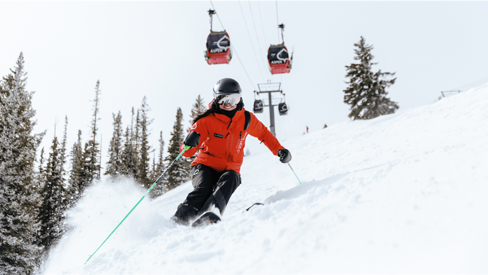 Ski Pro at Aspen Snowmass carves down a snowy hillside, under the aspen gondola
