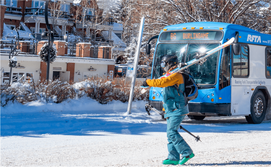 Man walks across the street with skies on his shoulder, in front of the RFTA free bus on a winter day