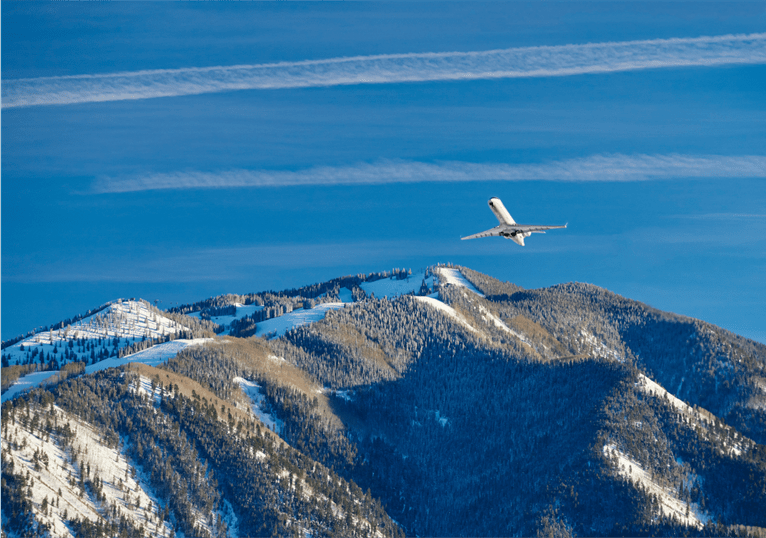 airplane flies over mountains in the town of aspen