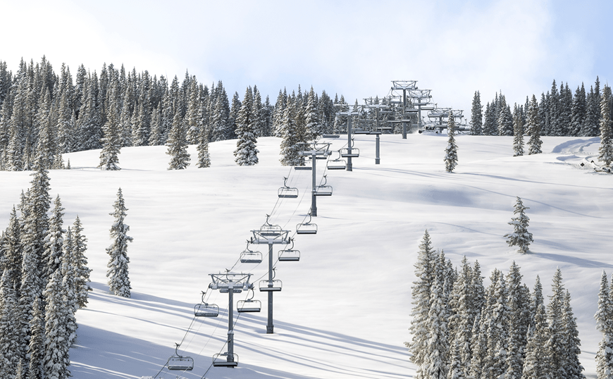 Big Burn lift traveling up a snowy ski slope, green pine trees are coated with snow under a bluebird ski day