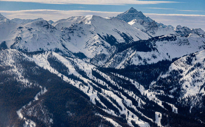 Arial view of snowmass, deep greens and blues contract the white ski runs and shadows of the dark trees and stark mountains