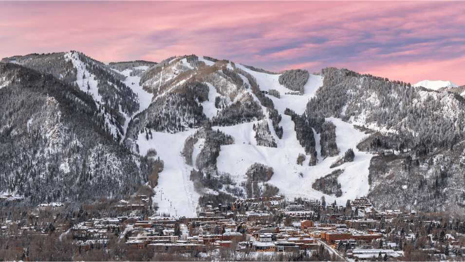 long shot of Aspen Mountain and town, pink skies above snowy white  ski runs, and a sleepy town at dusk