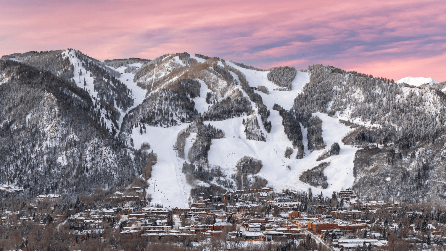 long shot of Aspen Mountain and town, pink skies above snowy white  ski runs, and a sleepy town at dusk