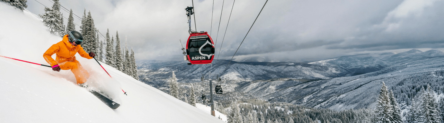 Skier is orange carves down powdery slope under the silver queen gondola on Aspen Mountain
