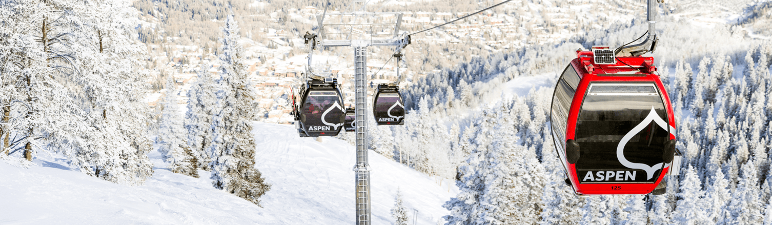 gondola cars move above snowy trees on a sunny powder day on Aspen Mountain