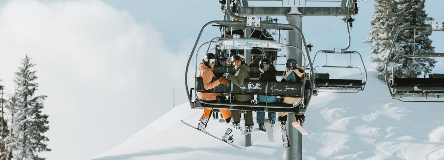 group of people smile back at the camera on the chairlift at Aspen Highlands