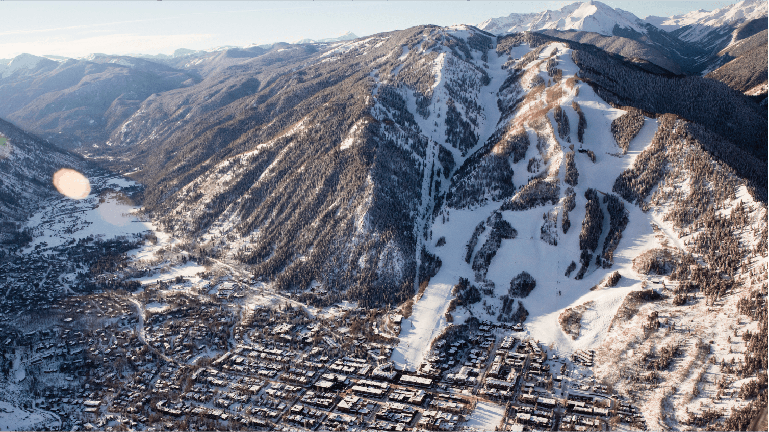 Aerial view of aspen mountain during morning sunrise, sun casts golden glow on town and snowy mountain