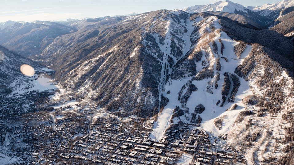 Aerial view of aspen mountain during morning sunrise, sun casts golden glow on town and snowy mountain
