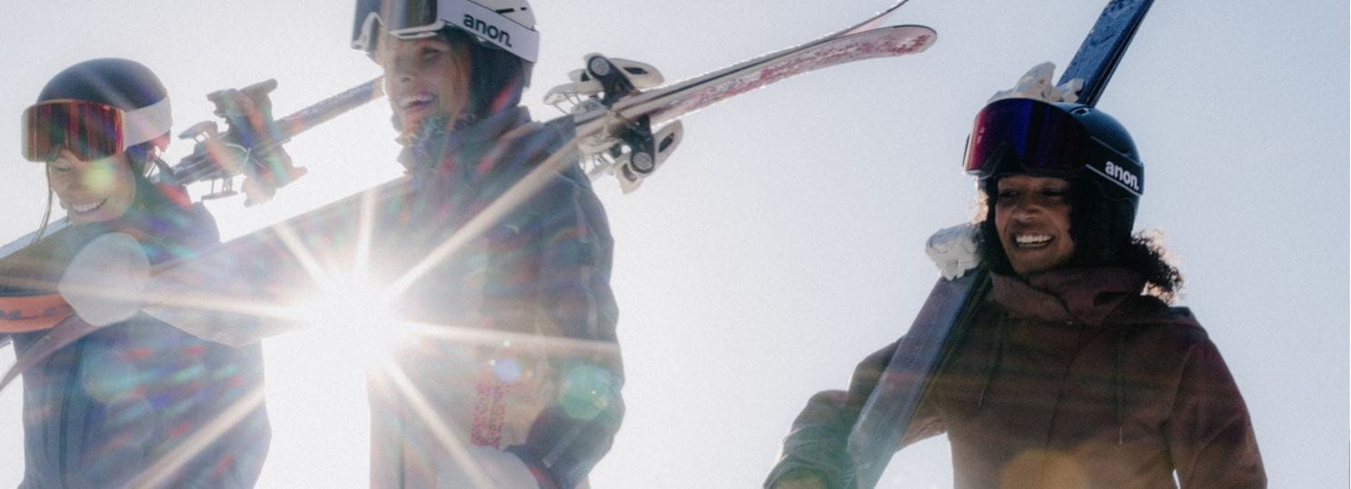 Three women walk with skies on shoulders, in aspen collection gear